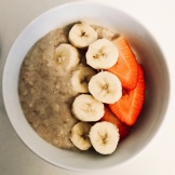Small bowl of porridge with 1 strawberry and a small banana.